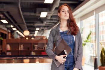 Portrait Of Casually Dressed Young Businesswoman Standing In Modern Open Plan Workplace