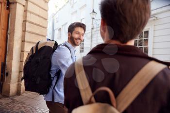 Rear View Of Male Gay Couple On Vacation Wearing Backpacks Walking Along City Street