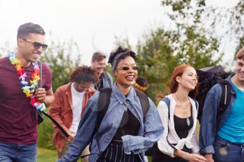 Group Of Excited Young Friends Carrying Camping Equipment Through Field To Music Festival