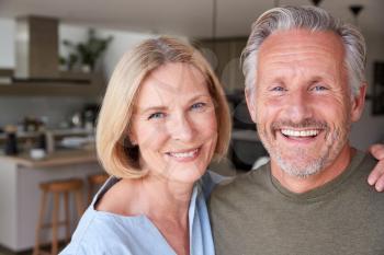 Portrait Of Smiling Senior Couple Standing At Home In Kitchen Together