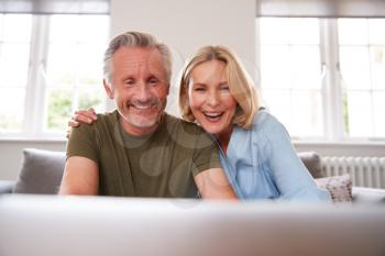 Senior Couple Sitting On Sofa In Lounge At Home Using Laptop Together