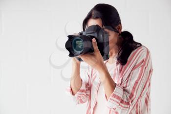 Female Photographer With Camera On Photo Shoot Against White Studio Backdrop
