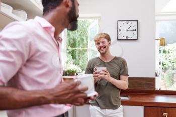 Male Same Sex Couple At Home Talking And Drinking Coffee In Kitchen Together