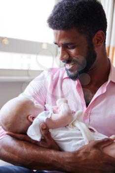 Loving Father In Armchair Cuddling Baby Daughter At Home