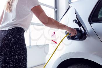 Close Up Of Woman Charging Electric Vehicle With Cable In Garage At Home