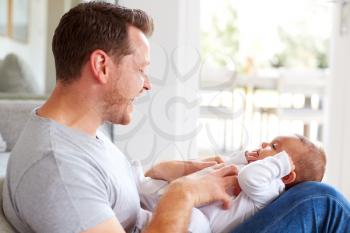 Baby Daughter Lying On Fathers Lap As He Plays Game With Her At Home
