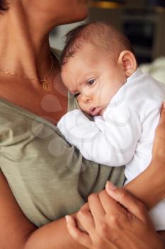 Close Up Of Loving Mother Holding 3 Month Old Baby Daughter In Kitchen At Home