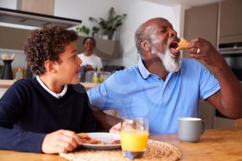 Grandparents Sitting In Kitchen With Grandson Eating Breakfast Before Going To School