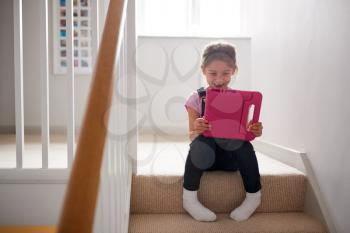 Girl Sitting On Stairs At Home Playing With Digital Tablet