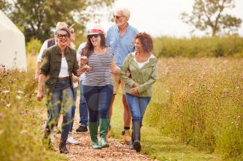 Group Of Mature Friends Walking Along Path Through Yurt Campsite