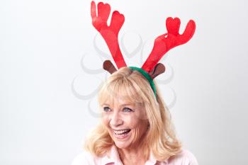 Studio Shot Of Happy Mature Woman Wearing Dressing Up Reindeer Antlers Against White Background