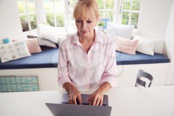 Mature Disabled Woman With Crutches At Home Working On Laptop On Kitchen Counter