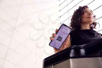 Businesswoman In Airport Departure Lounge Scanning Digital Boarding Pass On Smart Phone