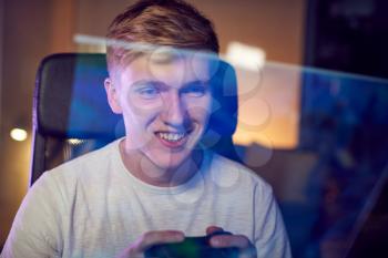Teenage Boy With Game Pad Sitting In Chair and Gaming At Home With Screen Reflection