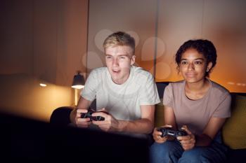 Teenage Couple Sitting On Sofa At Home Computer Gaming Together