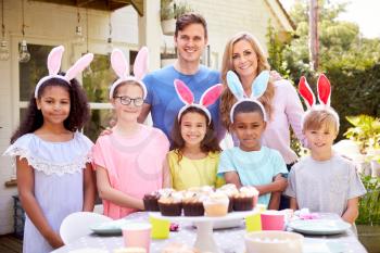 Portrait Of Parents With Children Wearing Bunny Ears Enjoying Outdoor Easter Party In Garden At Home