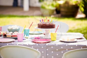 Table In Garden Laid For Childrens Birthday Party Including Cake With Candles
