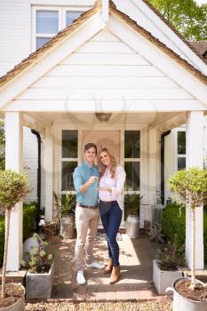 Portrait Of Couple Holding Keys To New Home Standing Outside Front Door