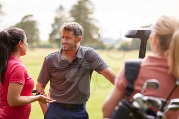 Group Of Male And Female Golfers Standing By Golf Buggy On Course