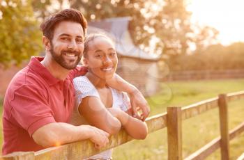 Portrait Of Romantic Couple Taking A Break And Resting On Fence During Walk In Countryside