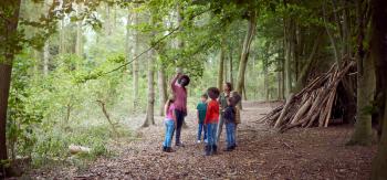 Adult Team Leaders With Group Of Children At Outdoor Activity Camp Walking Through Woodland