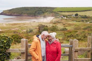 Loving Active Senior Couple Resting By Gate As They Walk Along Coastal Path In Winter