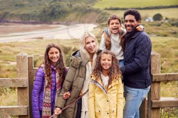 Portrait Of Active Multi-Cultural Family Standing By Gate On Winter Beach Vacation