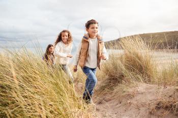 Three Children Having Fun Exploring In Sand Dunes On Winter Beach Vacation