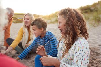 Multi-Generation Family Toasting Marshmallows Around Fire On Winter Beach Vacation