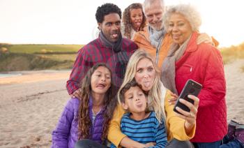 Multi-Generation Family Sitting By Fire On Winter Beach Vacation Taking Selfie