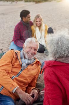 Loving Senior Couple Relaxing By Fire With Adult Offspring On Winter Beach Vacation