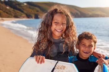 Portrait Of Children Wearing Wetsuits Holding Bodyboards On Summer Beach Vacation Having Fun By Sea