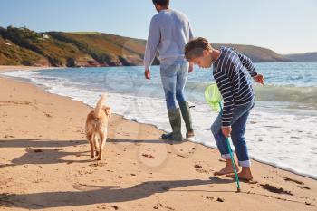 Father And Son With Dog Walking Along Beach By Breaking Waves On Beach Holding Fishing Net
