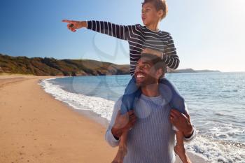 Loving Father Giving Son Ride On Shoulders As They Walk Along Beach Together
