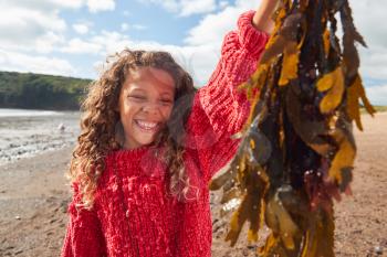 Portrait Of Smiling Girl Holding Seaweed On Winter Beach Vacation