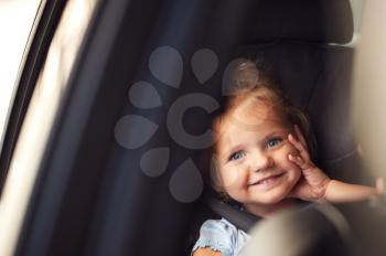 Portrait Of Young Girl Sitting In Child Safety Seat On Car Journey Looking Out Of Window
