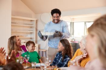 Father Serving Food As Multi-Generation Family Meet For Meal At Home