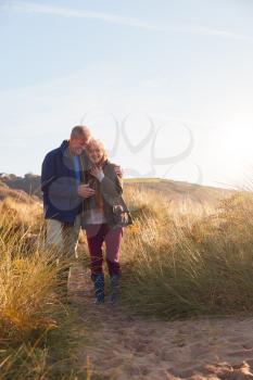 Loving Active Senior Couple Hugging As They Walk Through Sand Dunes