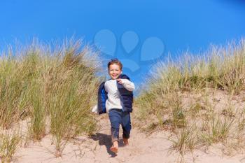 Young Boy Having Fun On Beach Vacation Running Down Sand Dunes