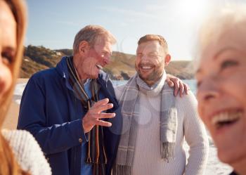 Senior Couple Walking Along Shoreline With Adult Offspring On Winter Beach Vacation