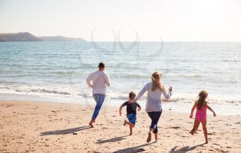 Rear View Of Family On Beach Running Across Sand Towards Sea