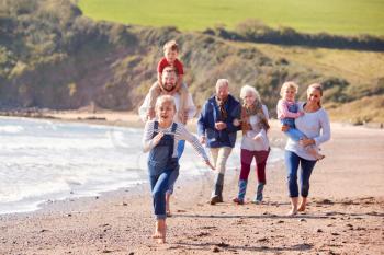 Multi-Generation Family Walking Along Shoreline Of Beach By Waves Together