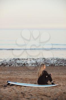 Rear View Of Thoughtful Woman Wearing Wetsuit On Surfing Staycation Looking Out To  Sea At Waves