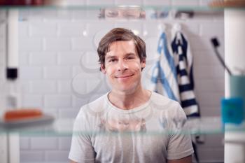 View Through Bathroom Cabinet Of Smiling Man Looking In Mirror Before Going To Work