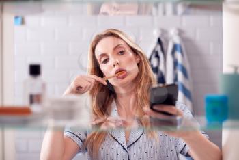 View Through Bathroom Cabinet Of Woman Brushing Teeth And Checking Phone Before Going To Work