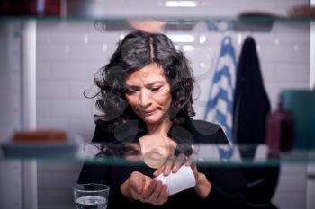 View Through Bathroom Cabinet Of Mature Woman Taking Medication From Container