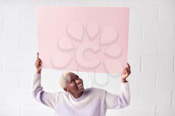 Happy Young Woman Holding Blank Pink Card With Copy Space Above Head White Against White Studio Wall