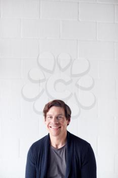 Portrait Of Casually Dressed Smiling Man Standing Against White Studio Wall