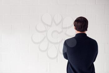 Rear View  Of Casually Dressed Man Standing Against White Studio Wall