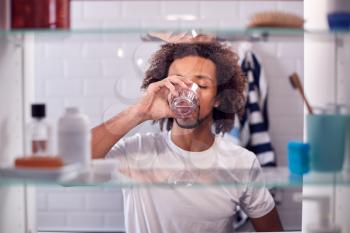 View Through Bathroom Cabinet Of Man Drinking Glass Of Water